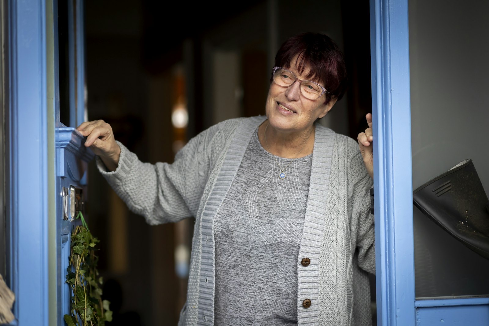 A smiling woman opening her blue front door.