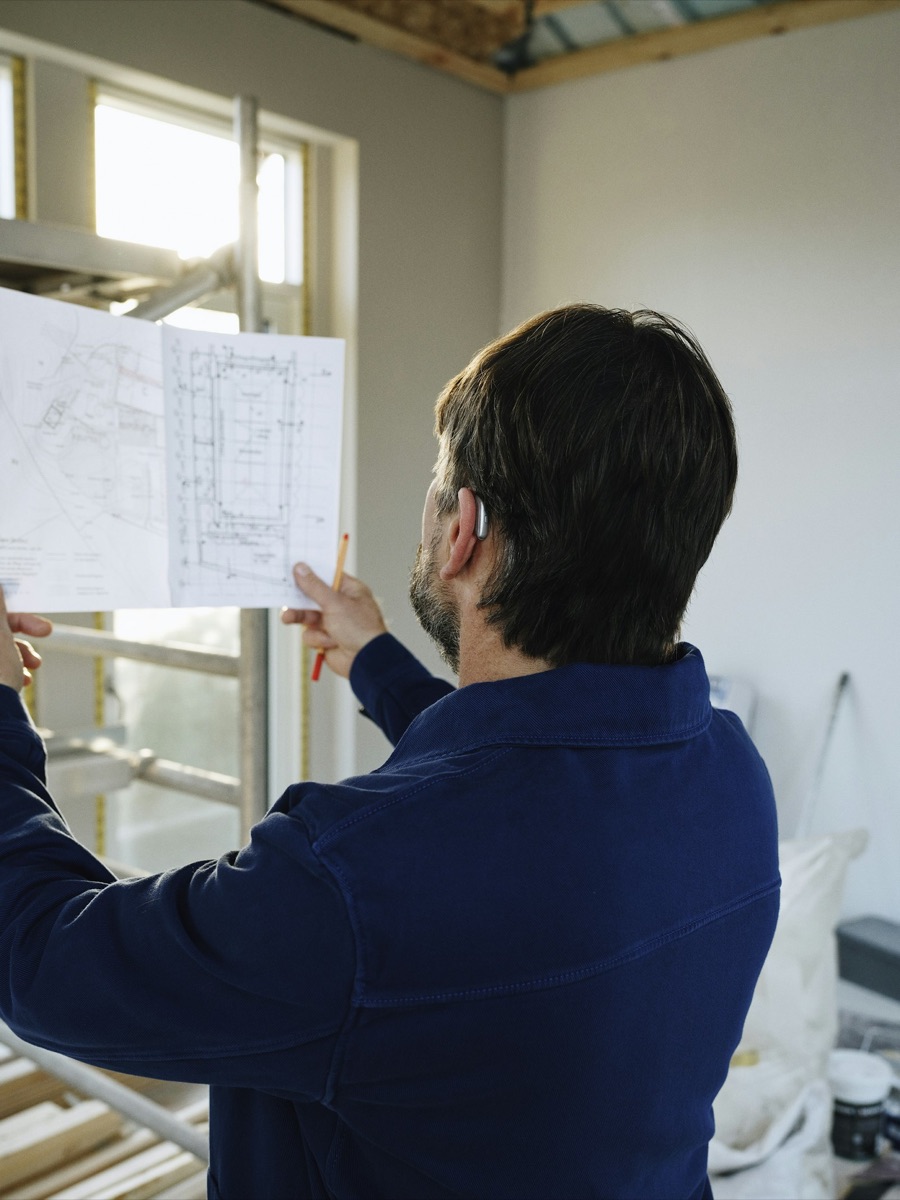 A builder holding up a set of plans in a half-finished room.